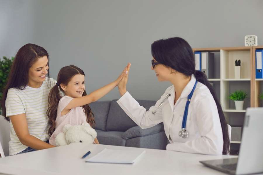 Une petite fille fait un check-up avec sa mère en souriant et en consultant un pédiatre dans un cabinet médical.
